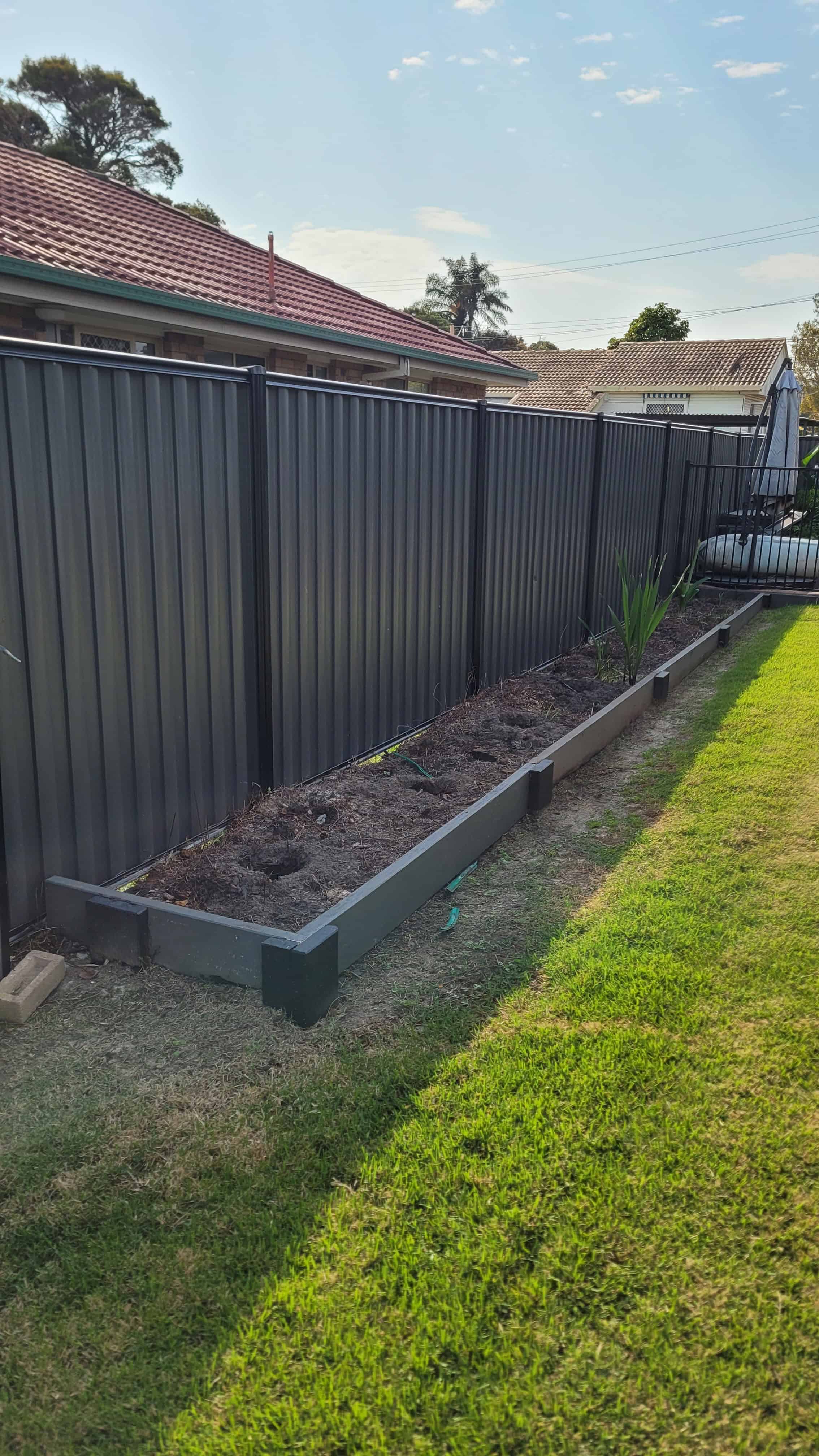 A long raised garden bed full of nothing but dirt and weeds.