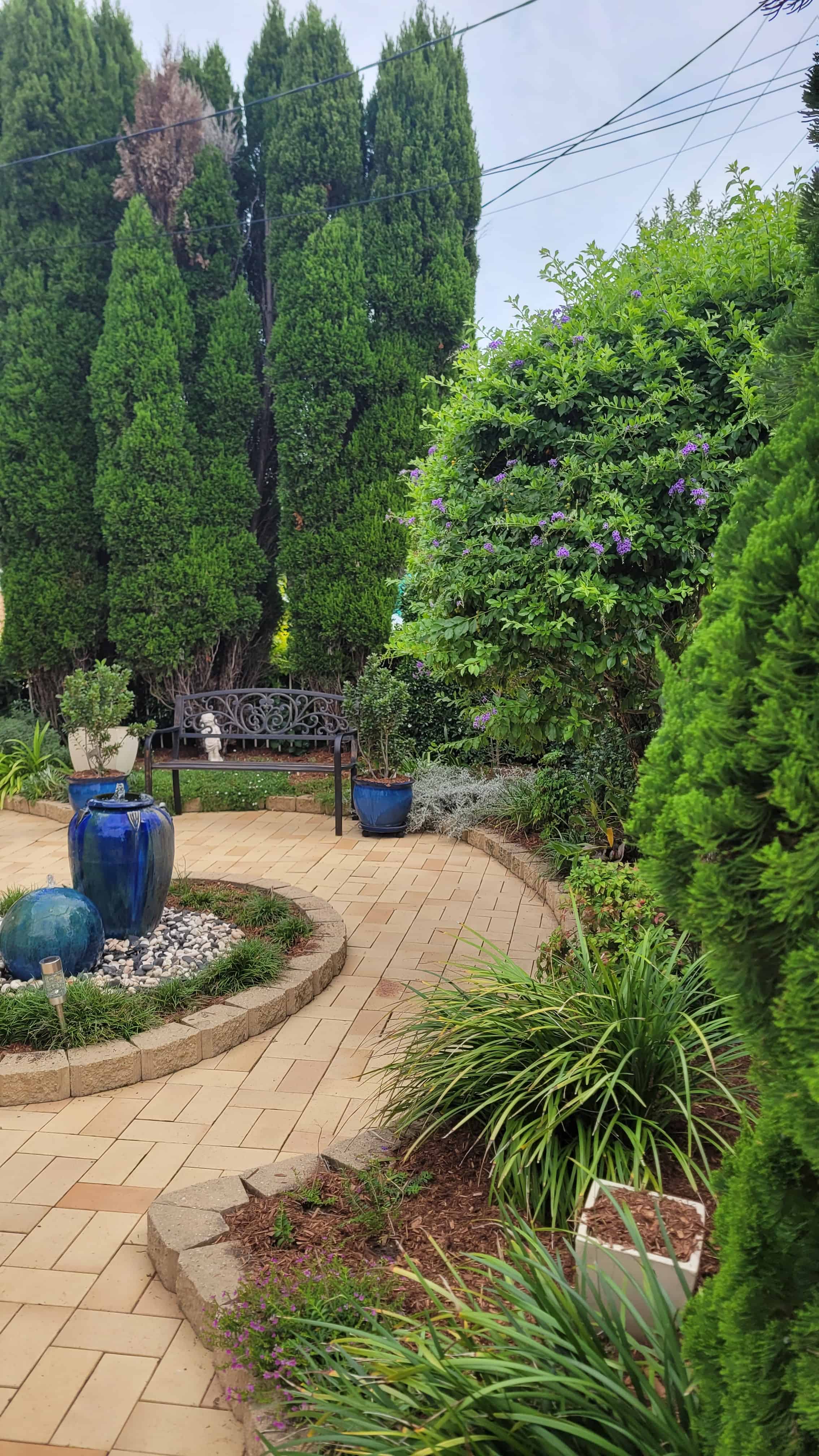 A garden courtyard with a winding path, blue water feature and established planting.
