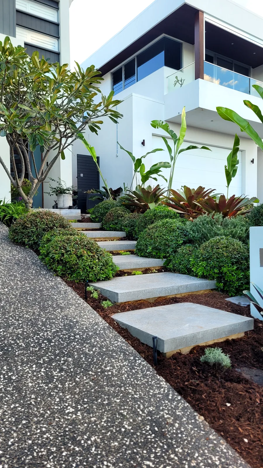 Fresh mulch and neatly shaped shrubs surrounding stone steps in a front garden.